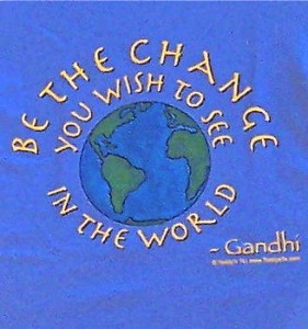 Light blue shirt with gold lettering “You must be the change…” surrounding a hand drawn globe hand painted in blue and green by Teddy.